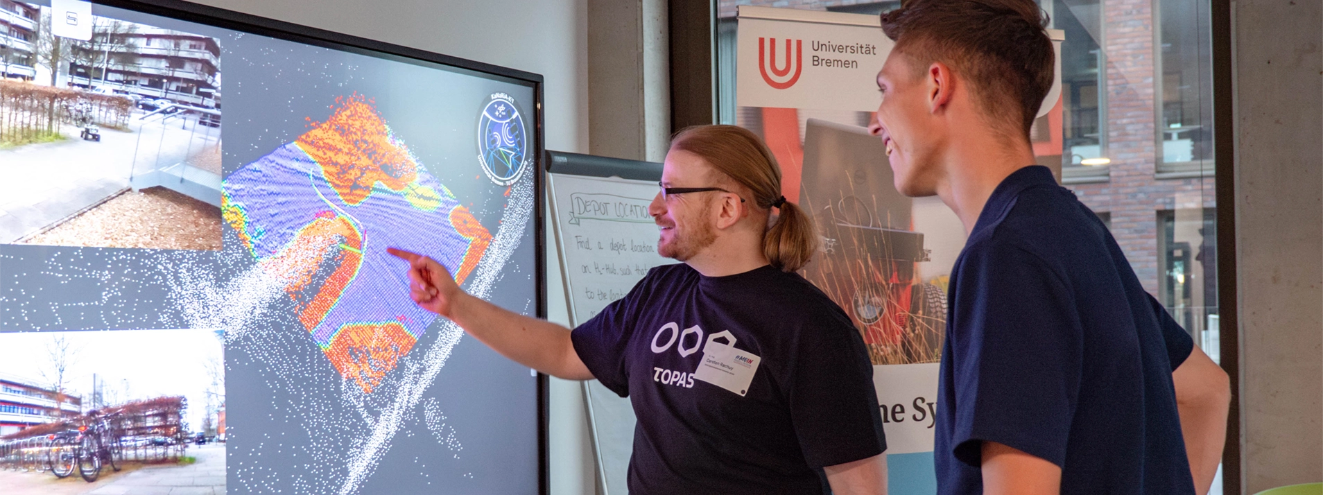 Zwei Männer betrachten eine 3D-Datenvisualisierung auf einem Bildschirm bei einer Präsentation an der Uni Bremen.